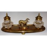 A brass inkwell with original cut glass wells, oval shaped brass base set with a dog, four bun feet,