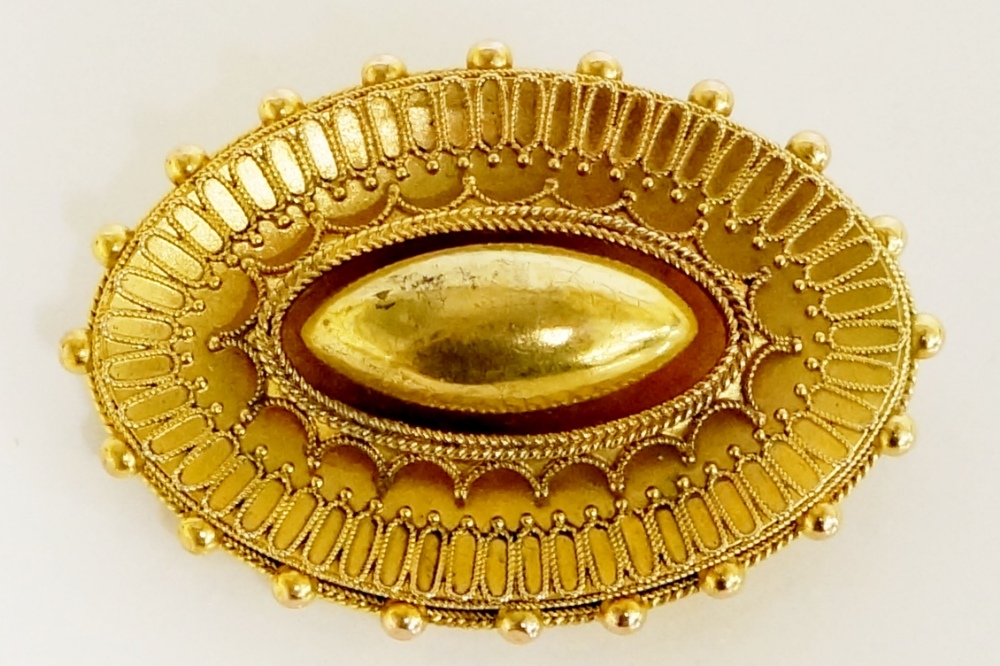 A Victorian gold brooch of oval design with raised centre above an inverted crown frame and outer
