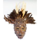 A small decorative African tribal mask applied shells and beads with studded decoration and feather