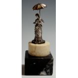 A white metal figure of a Victorian lady holding a parasol on a stepped marble base in cream and