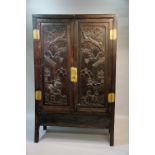 A Chinese hardwood cupboard of panelled construction enclosed by a pair of  doors finely carved