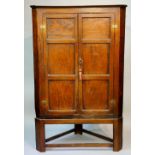 A George III elm corner cupboard on stand the shallow cornice above three panelled doors enclosing