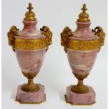 A pair of gilt metal mounted pink marble urns of classical design with domed finials,