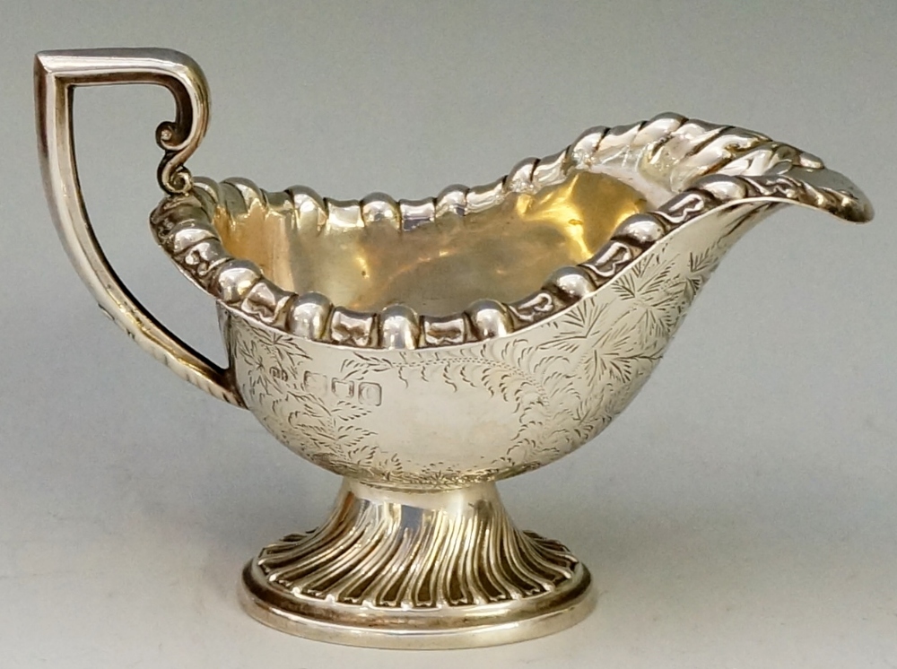 A late Victorian cream jug, boat shaped, with stylised foliate rim and C-scroll handle,