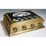 A gilt metal and pietra dura games box the hinged lid inset with a black slate panel inlaid with