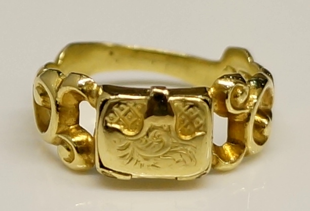 A Victorian gold pill box ring with central hinged "satchel", pierced S-scroll leafy shoulders,