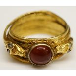 An antique gold coloured metal ring with central red stone cabochon flanked by a pair of