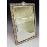 A late Victorian silver mirror frame the border embossed with scrolls and leafage the arched top