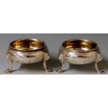 A pair of George III cauldron shaped salts with foliate and shell engraved bodies,