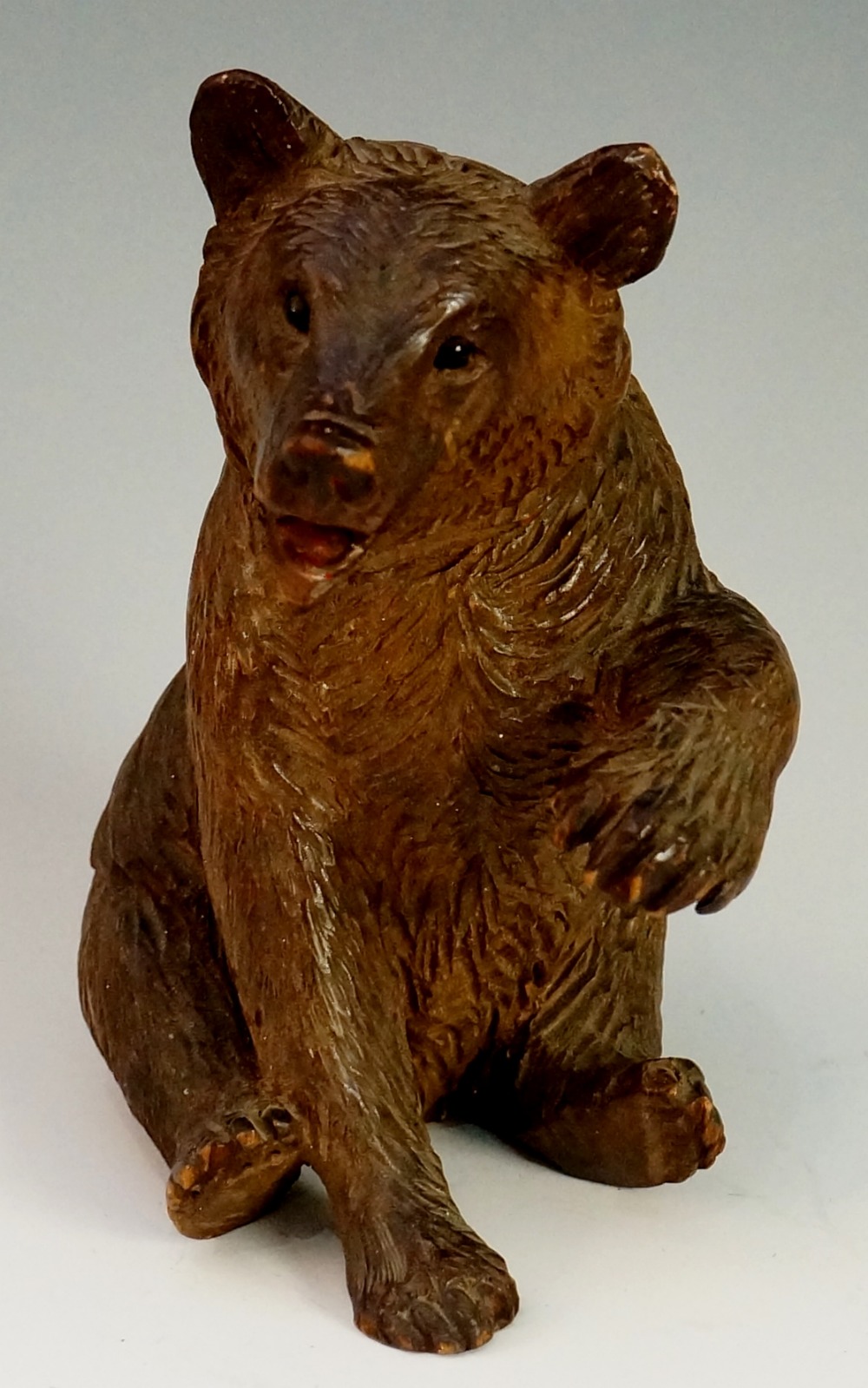 A seated bear its left paw outstretched, glass eyes and open mouth, 15cm high,