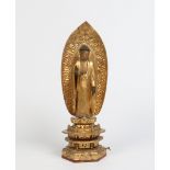 An Oriental carved gilt wood figure of a Buddha. Stood over a hexagonal plinth before an arched