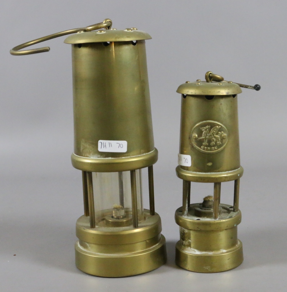 A brass cased miners lamp along with a smaller brass miners lamp.