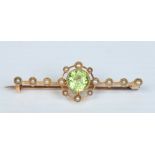 A Victorian 15 carat gold bar brooch. Set with a faceted circular peridot stone and fourteen seed