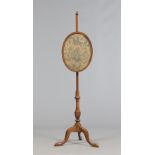 A Victorian mahogany oval pole screen raised on a tripod base and embroidered with flowers and