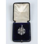 A cased early twentieth century white gold and diamond flower brooch / pendant. With a central