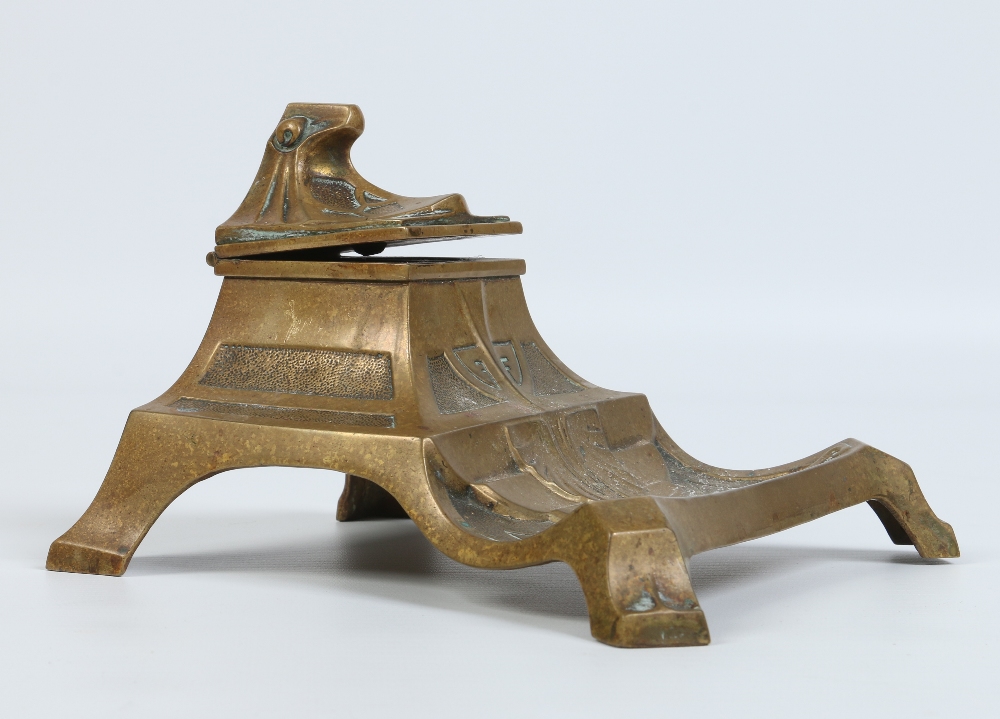 An Art Deco bronze desk stand with hinged cover incorporating an inkwell. Raised on bracket feet,