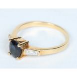 An Art Deco style 18 carat gold ring set with an ovoid sapphire flanked by a pair of trapeze cut