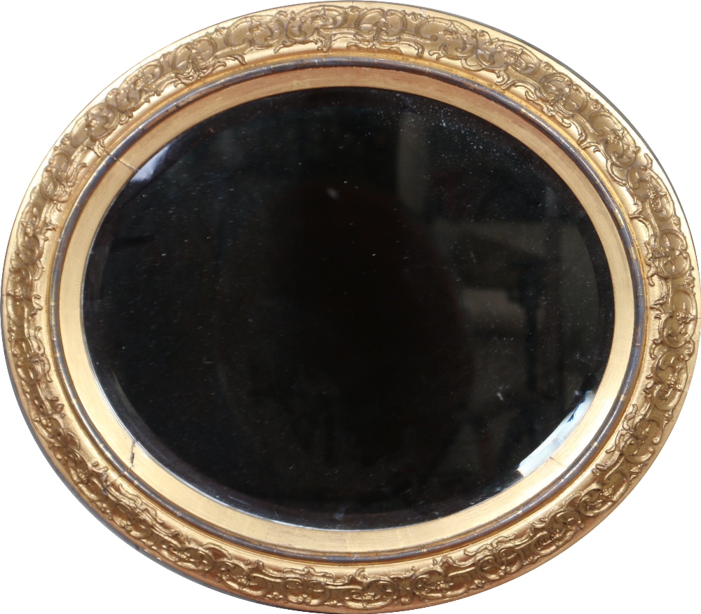 An early twentieth century oval bevel edged wall mirror in moulded gilt frame ornamented with