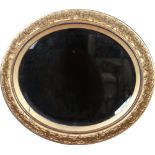 An early twentieth century oval bevel edged wall mirror in moulded gilt frame ornamented with