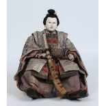 A Japanese doll formed as a Samurai warrior and with silk embroidered clothing and miniature sword,