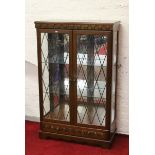 A carved oak lead glazed display cabinet with mirrored back and base drawer.