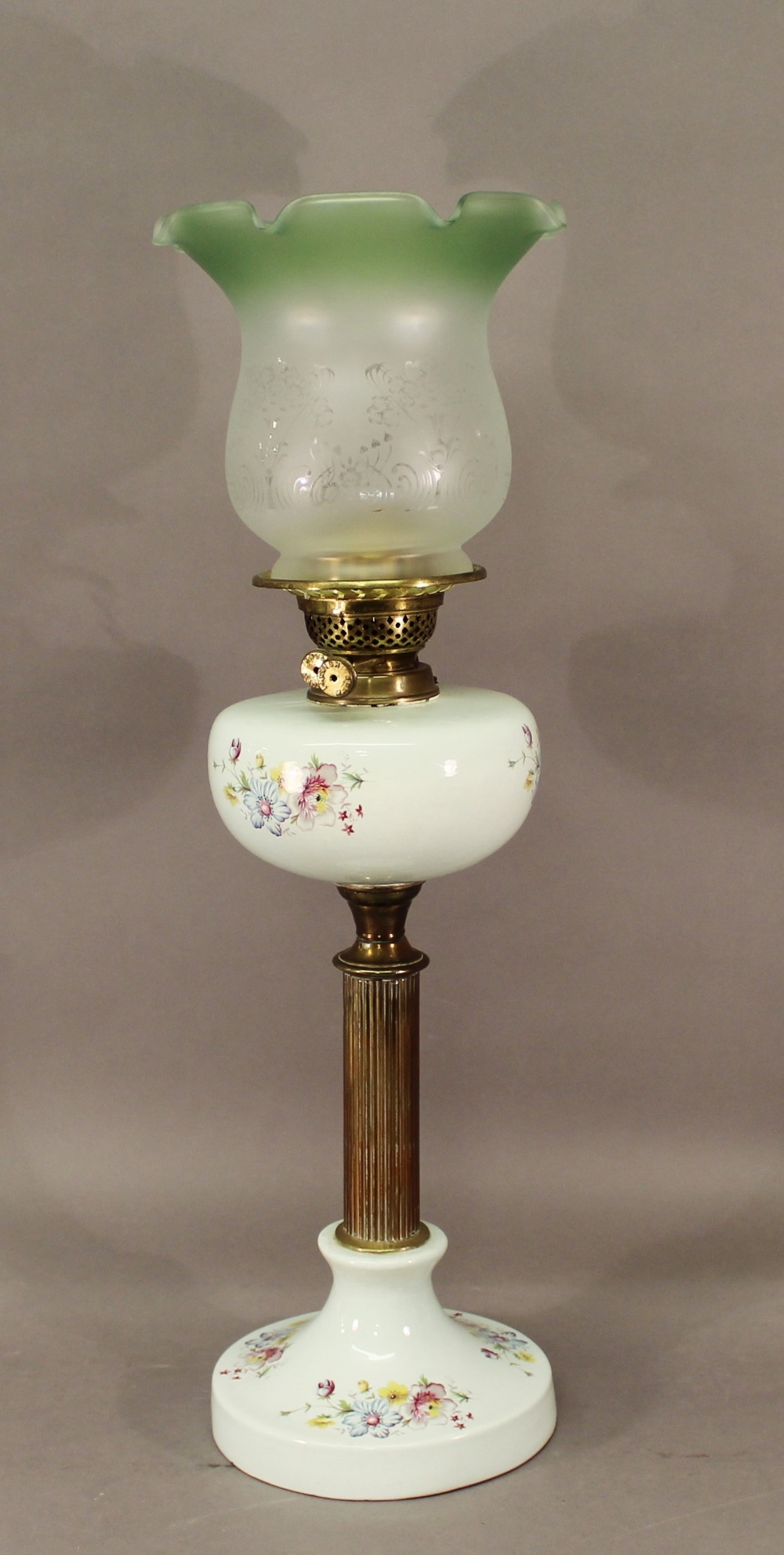 A 20TH CENTURY BRASS AND CERAMIC COLUMN OIL LAMP having a green tinted etched glass shade, brass