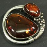 A WHITE METAL AND AMBER BROOCH of stylised foliate form with two amber cabochons, unmarked. 5cm,