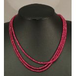 A FACET-CUT RUBY NECKLACE having three strings of multiple facet-cut and graduating stones finishing