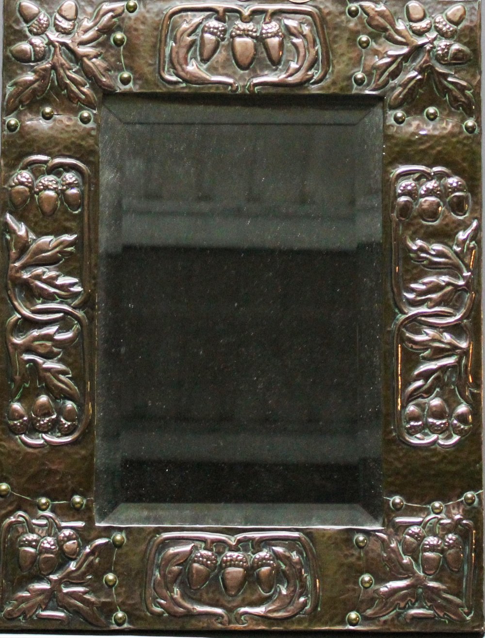 AN ARTS AND CRAFTS COPPER FRAMED MIRROR having a bevelled rectangular plate in a hand-beaten and
