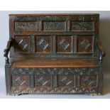 AN EARLY 18TH CENTURY (AND LATER) CARVED OAK BOX SETTLE having a moulded top-rail, carved S-scroll