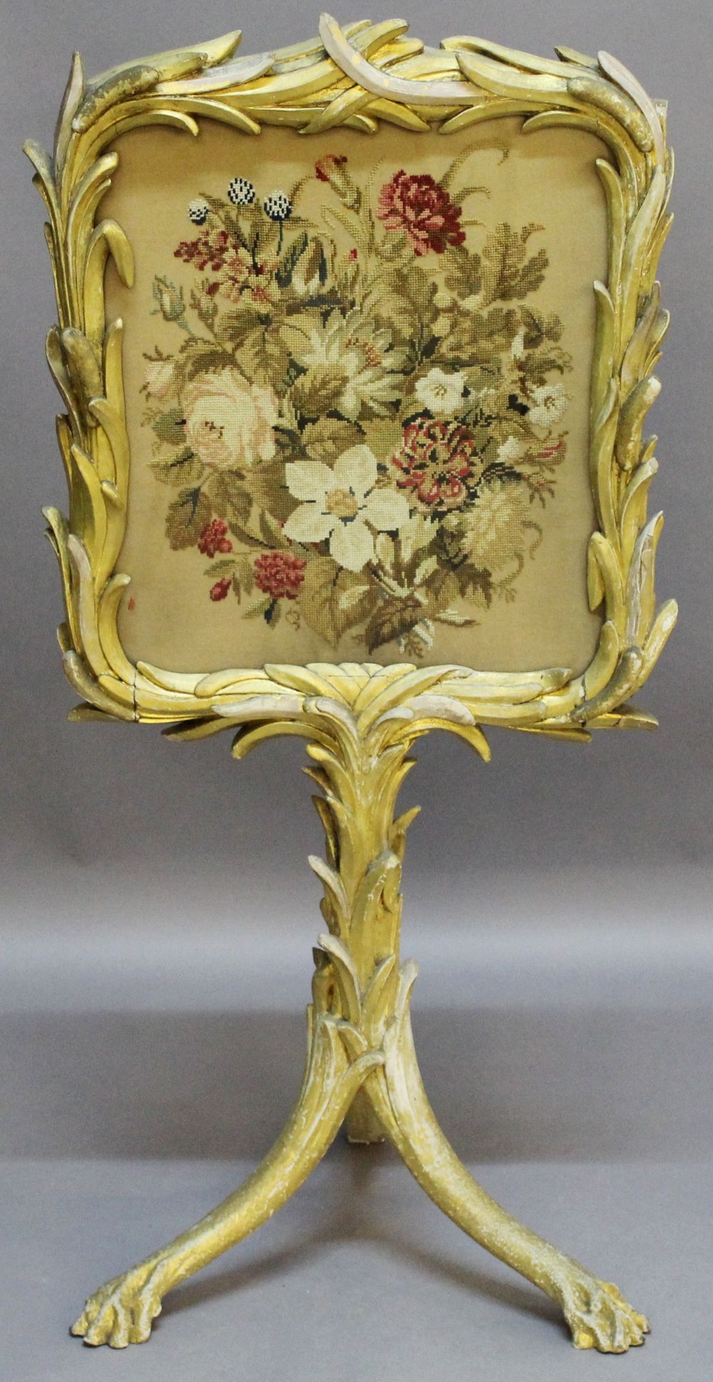 A 19TH CENTURY GILT-WOOD FIRESCREEN the floral needlework panel within a foliate giltwood