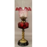 A VICTORIAN BRASS AND GLASS OIL LAMP having a ruffled cranberry tinted shade, brass Duplex burner