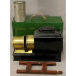 A MAGIC LANTERN PROJECTOR with black tin body and brass lens housing, complete with green tin case