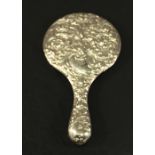 AN EDWARDIAN SILVER-BACKED HAND MIRROR of typical form with embossed cherub and scrolling foliate