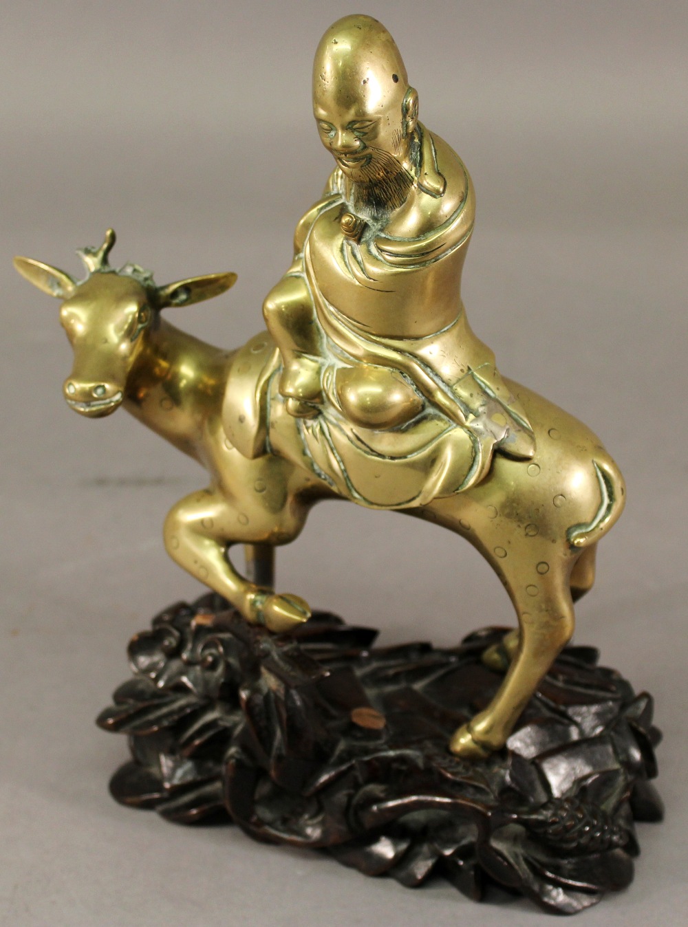 A CHINESE BRASS FIGURE of a Taoist man riding a deer, raised on a carved and pierced hardwood stand.
