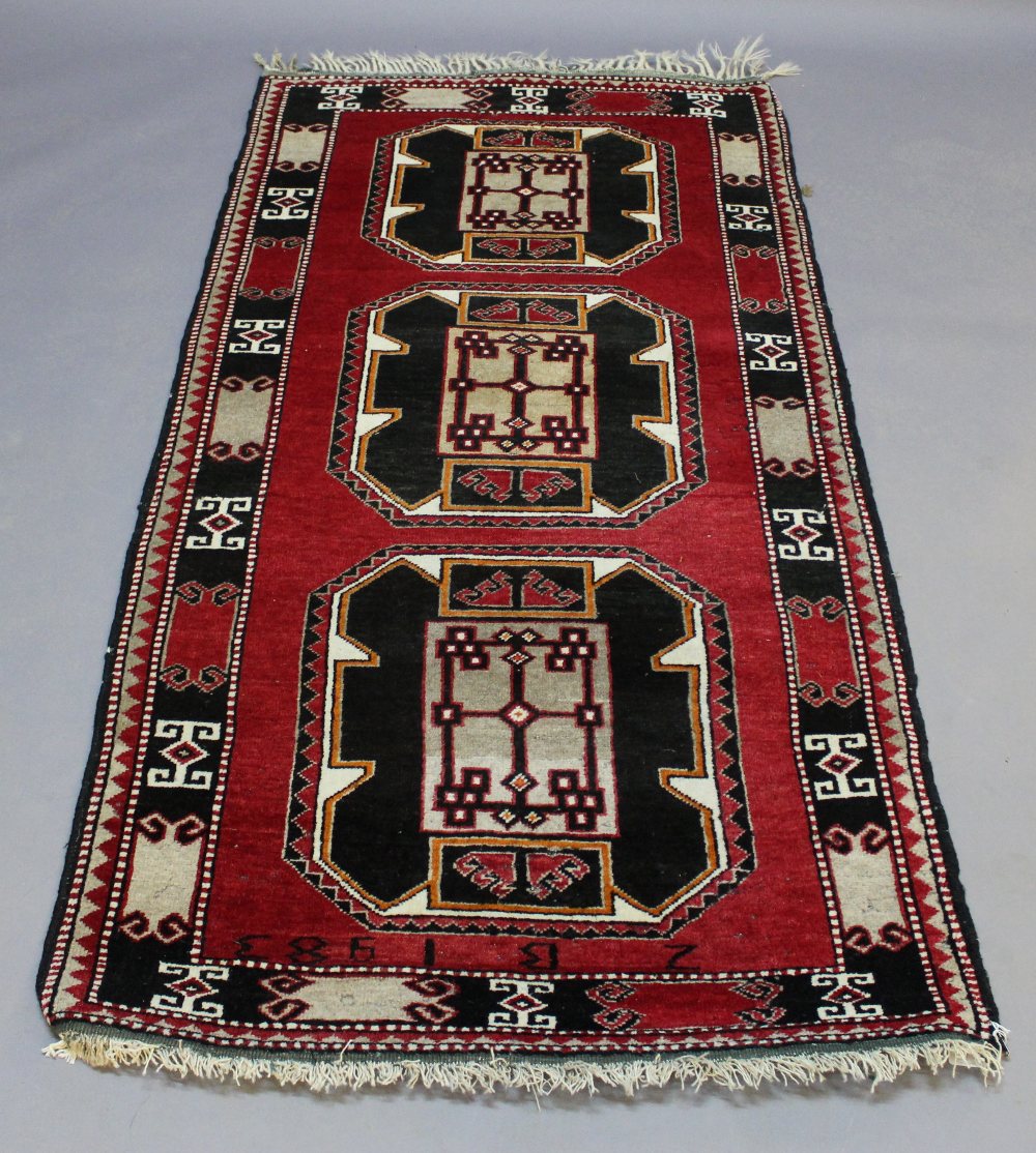 A WESTERN ANATOLIAN RUG, the vibrant red field filled with three large guls and enclosed by stylised