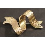 A VICTORIAN YELLOW METAL BROOCH in the form of a ribbon with engraved foliate decoration, the