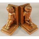 A PAIR OF CARVED MAHOGANY BOOKENDS carved as putti or young children leaning on upturned books.