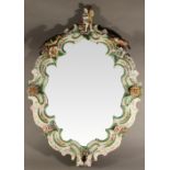 A 19TH CENTURY CONTINENTAL PORCELAIN-FRONTED WALL MIRROR of shaped oval form with figural crest