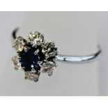 A 14K WHITE GOLD DIAMOND AND SAPPHIRE CLUSTER RING, the central round-cut sapphire set within six