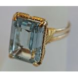 A YELLOW METAL AND AQUAMARINE COLOURED STONE RING, the large emerald-cut blue stone claw-set over