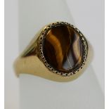 A 9CT GOLD TIGERS EYE SIGNET RING the oval polished stone in a geometric setting between tapering