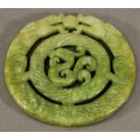 A CARVED AND PIERCED CHINESE GREEN STONE PLAQUE, circular, carved with dragons around a fluted
