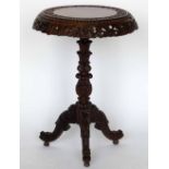 A Burmese carved hardwood tripod table, the circular tip-top with a foliage rim on an ornate central