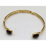 9ct gold slave bangle with two red stone terminals, 12.9g gross.