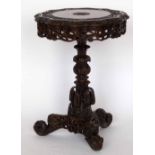 A Burmese hardwood circular table carved with foliage on an ornate central column and tri-point