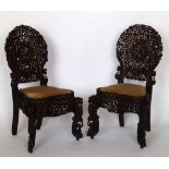 Pair of Burmese carved hardwood chairs, decorated with scrolling foliage and upholstered drop-in