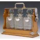 Oak tantalus with plated mounts enclosing three square decanters with silver labels, length 36cm (