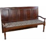 Oak settle, 19th century, the back of five raised panels over an upholstered seat on turned legs,