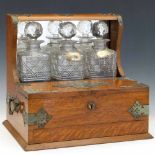Oak tantalus with applied cut metal mounts, a box front and drawer base enclosing three decanters,